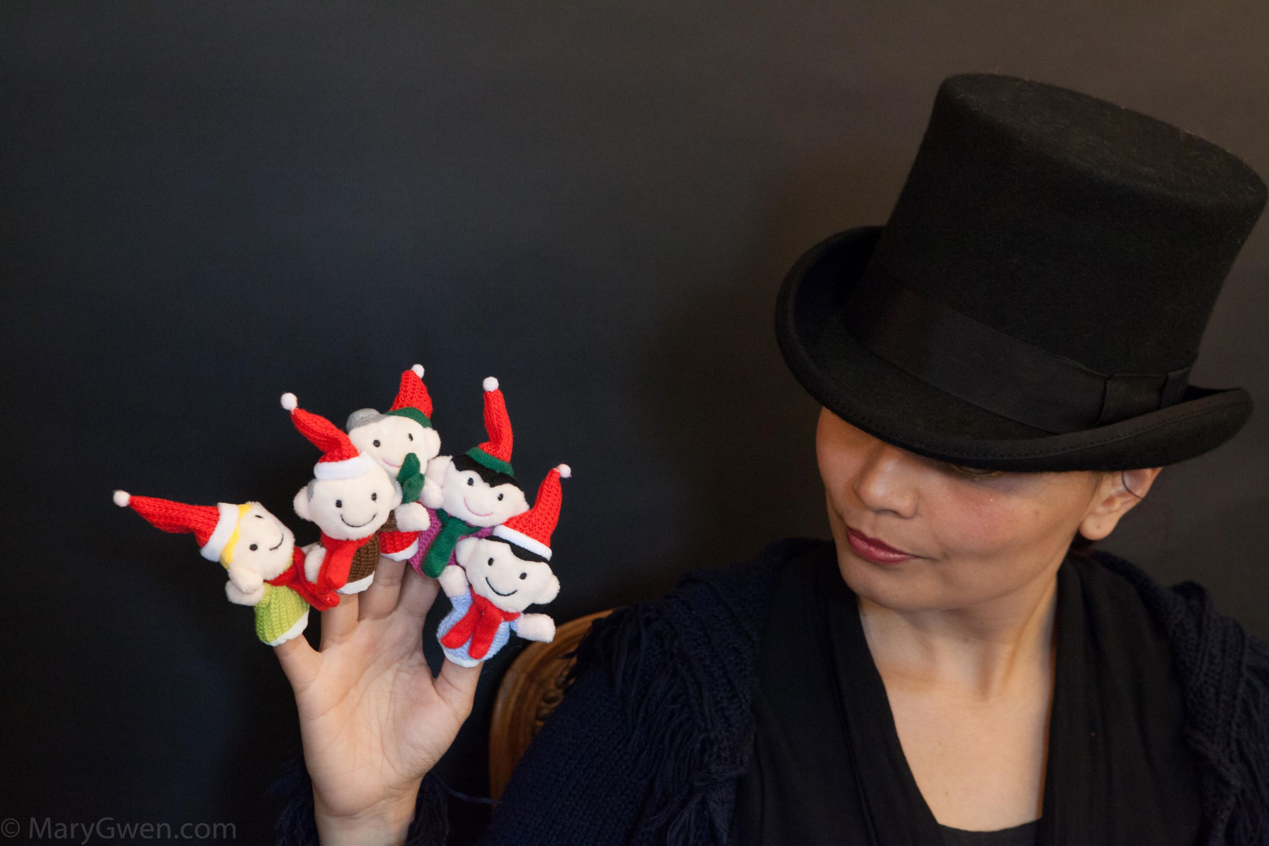 A person wearing a top hot holds up her hand, on each finger there is a finger puppet.