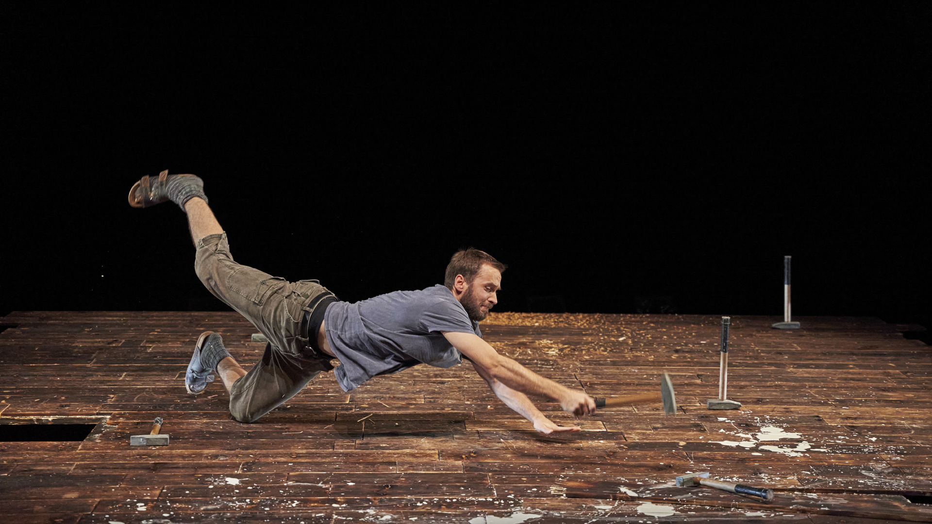 A person is jumping across a stage with a woodworking tool in his hand.