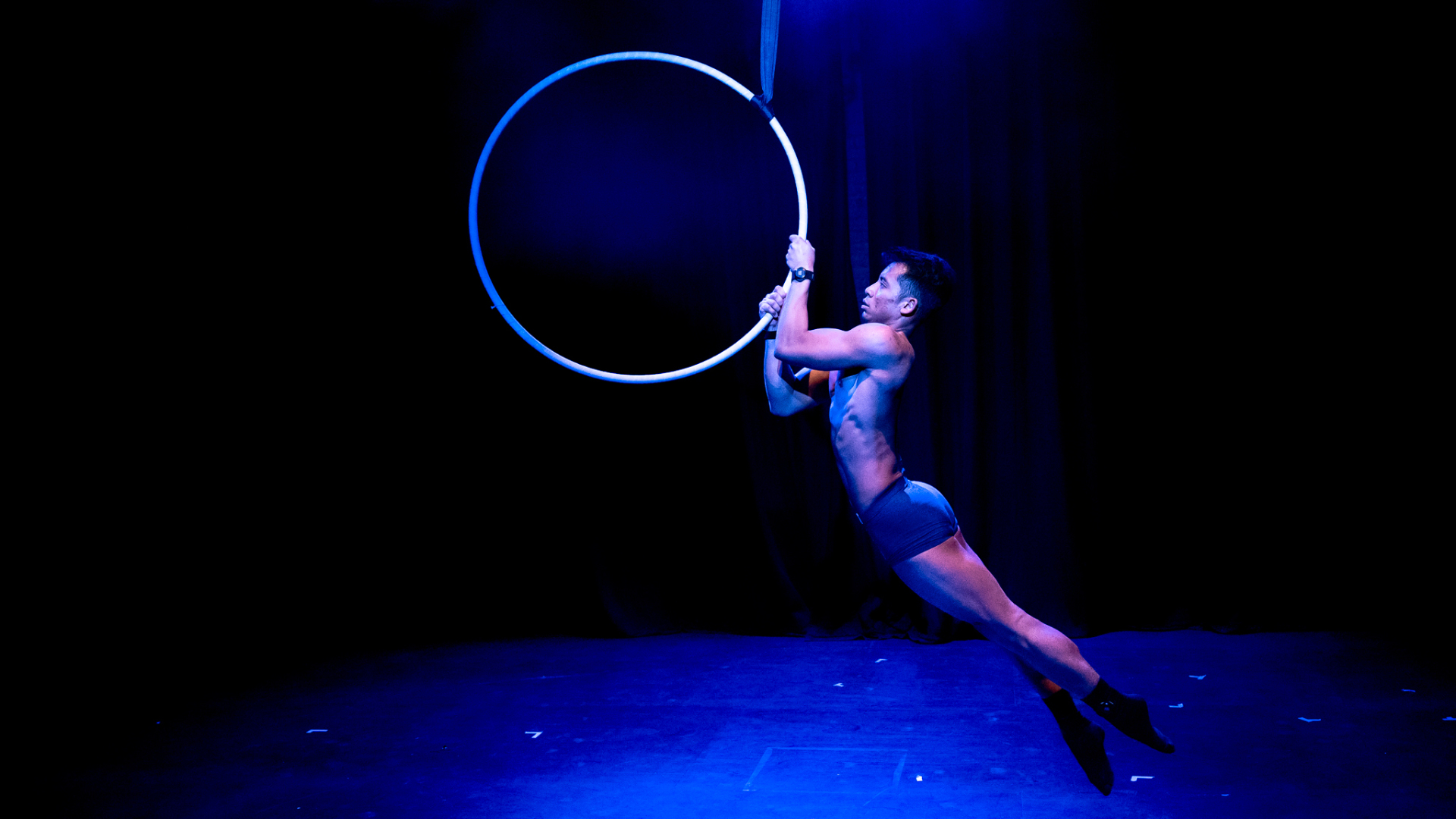 A person hangs from an aerial hoop.