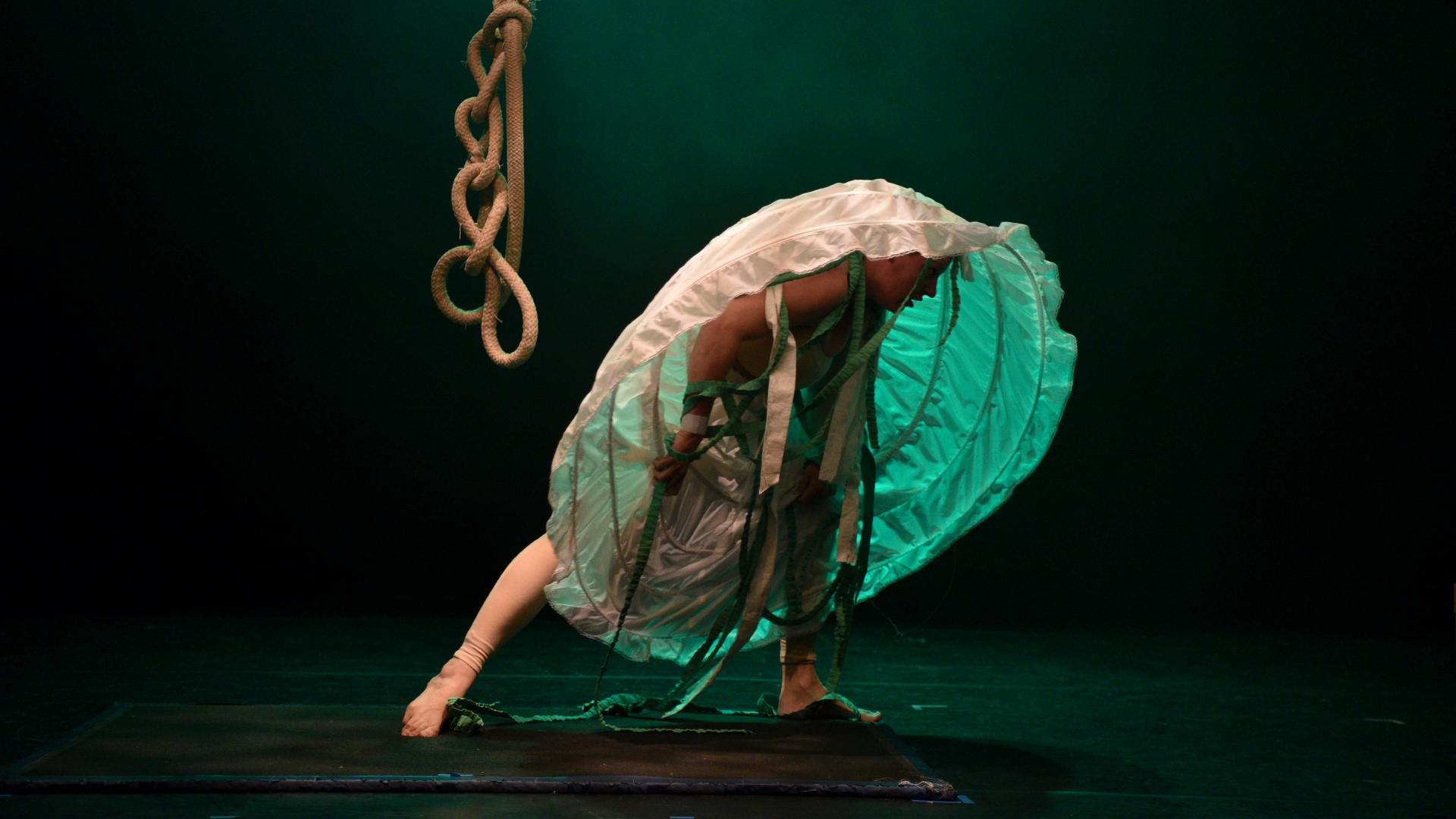 A person is crouching with an underskirt pulled over their head, a rope hangs in the background.