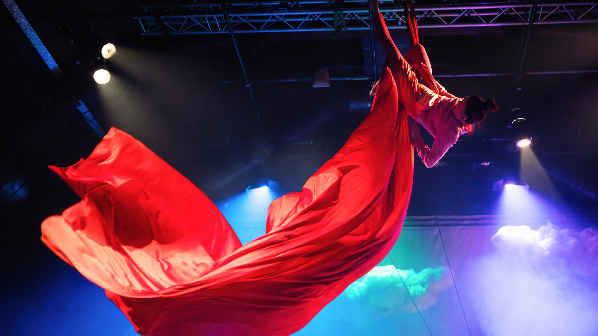 A person hangs upside down on red silks.